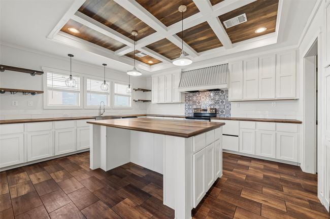 Kitchen featuring open shelves, white cabinetry, wall chimney range hood, coffered ceiling, and butcher block counters | Image 7