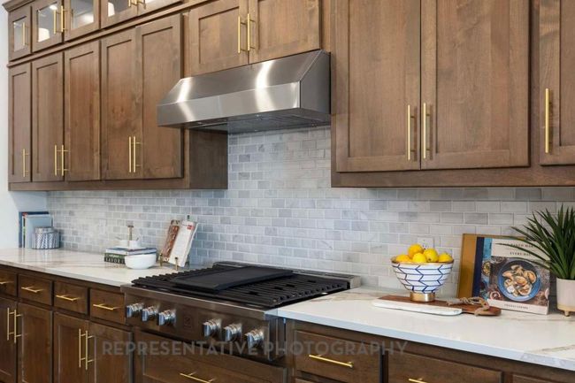 Kitchen with wall chimney exhaust hood, stainless steel gas cooktop, tasteful backsplash, and glass insert cabinets | Image 6