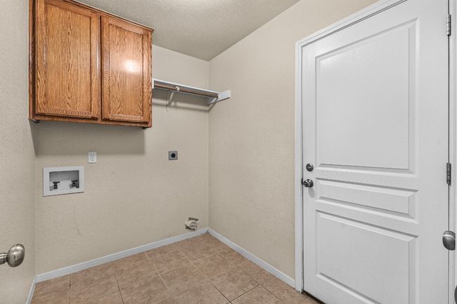 Washroom featuring hookup for a washing machine, cabinet space, hookup for an electric dryer, light tile patterned floors, and a textured ceiling | Image 7