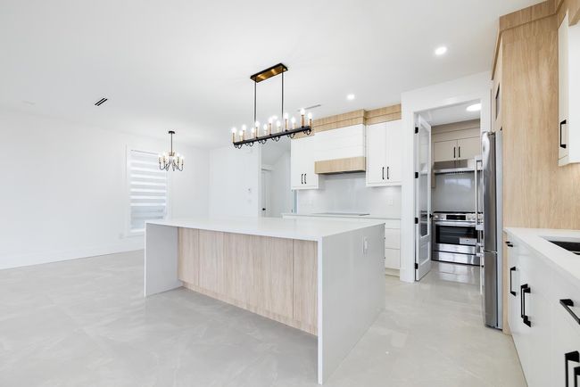 Kitchen with modern cabinets, a large island, a chandelier, light countertops, and recessed lighting | Image 12