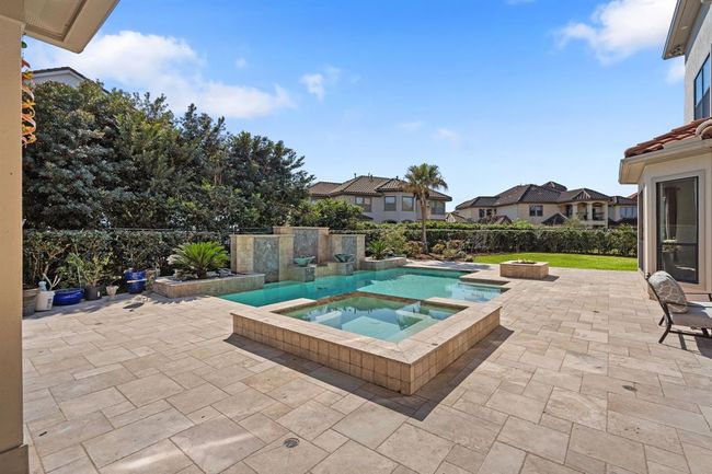 Stunning pool and spa surrounded by lush landscaping and a metal fence lined with vibrant shrubs. Pool fountains add a touch of tranquility, creating a private oasis perfect for relaxation and entertainment. | Image 49