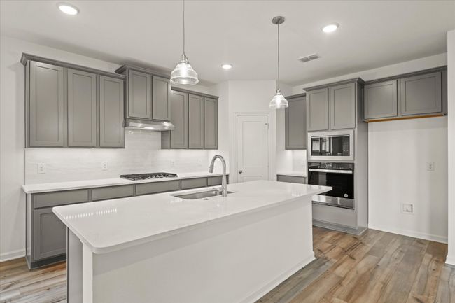 Kitchen featuring appliances with stainless steel finishes, under cabinet range hood, light wood-style flooring, decorative backsplash, and light countertops | Image 16