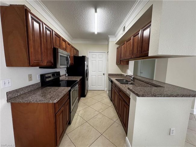 Kitchen featuring appliances with stainless steel finishes, a textured ceiling, dark countertops, and a sink | Image 13