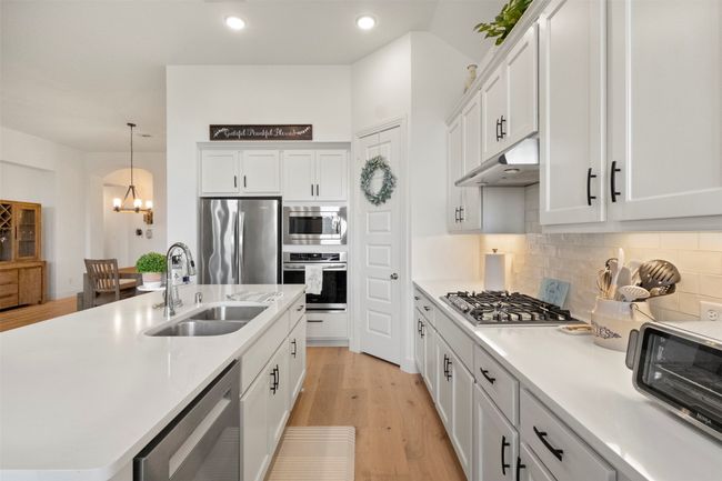 Kitchen with appliances with stainless steel finishes, under cabinet range hood, a chandelier, white cabinets, and recessed lighting | Image 25
