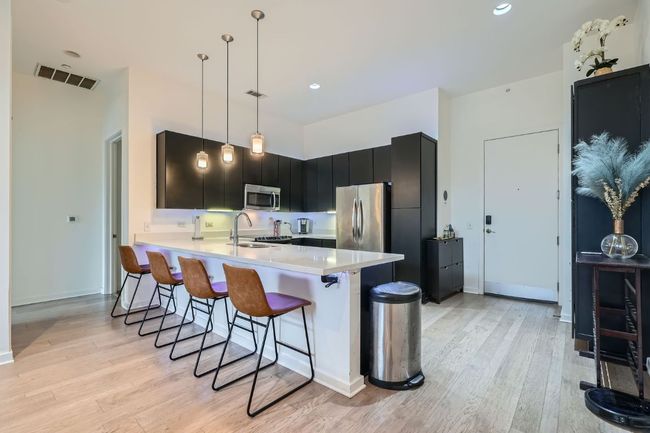 Kitchen with light countertops, visible vents, appliances with stainless steel finishes, dark cabinets, and a breakfast bar area | Image 12