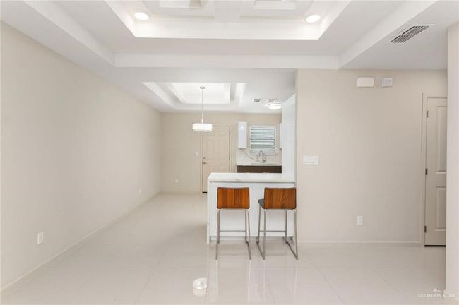 Kitchen with a tray ceiling, a kitchen breakfast bar, light tile patterned floors, and hanging light fixtures | Image 7