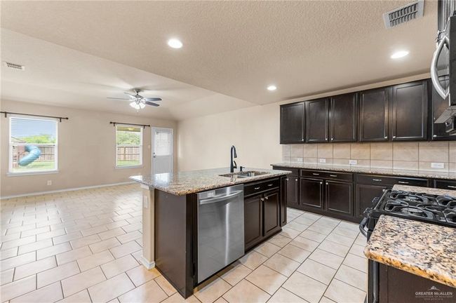 Kitchen featuring dishwasher, ceiling fan, decorative backsplash, an island with sink, and light stone countertops | Image 6