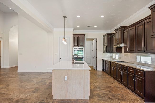 Kitchen with decorative backsplash, a kitchen island with sink, arched walkways, hanging light fixtures, and quartzite counters | Image 19
