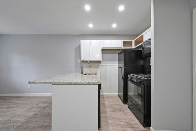 Kitchen featuring white cabinets, light wood-style flooring, recessed lighting, light stone counters, and black appliances | Image 13