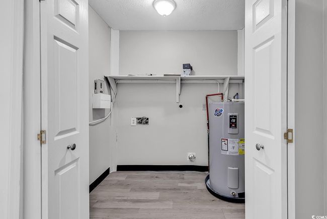 Washroom with electric water heater, hookup for an electric dryer, light wood-style floors, a textured ceiling, and hookup for a washing machine | Image 13
