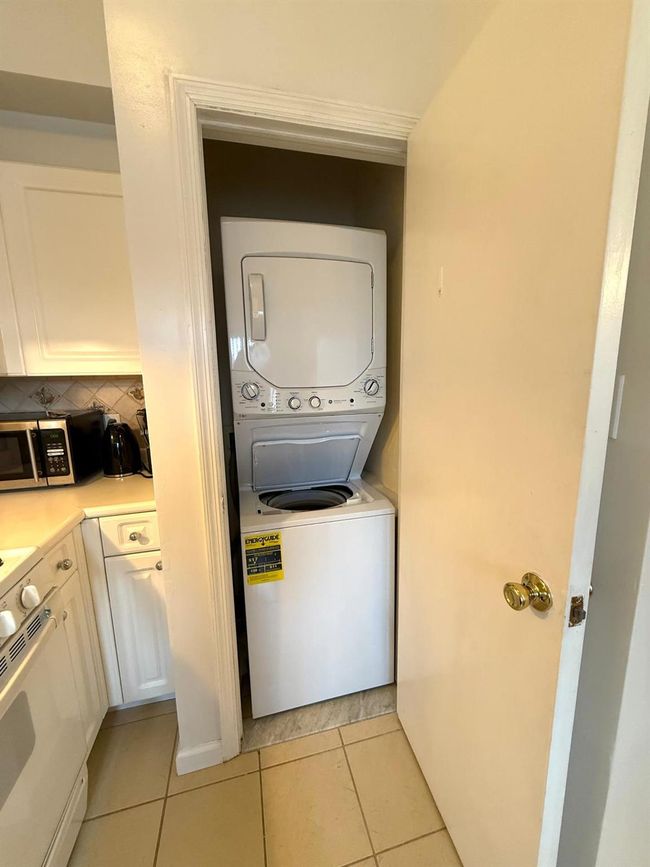 Washroom with stacked washing maching and dryer, light tile patterned floors, and laundry area | Image 10
