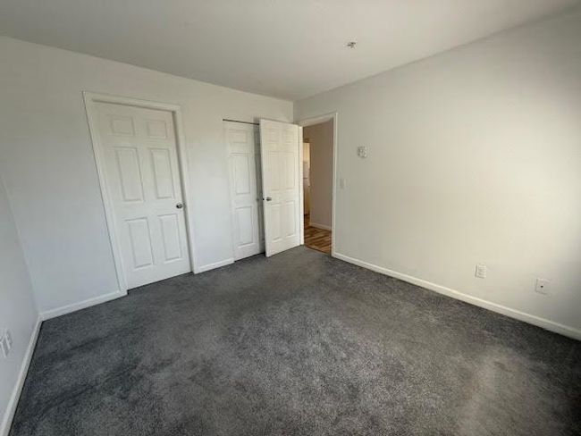 Unfurnished bedroom with a closet, baseboards, and dark carpet | Image 9