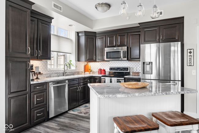 Updated kitchen featuring a breakfast bar, two toned cabinetry, stainless steel appliances, LVP & granite counters | Image 13