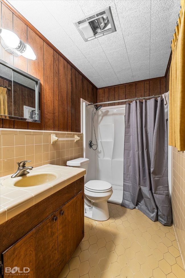 Full bathroom featuring vanity, tile walls, curtained shower, toilet, and wooden walls | Image 19