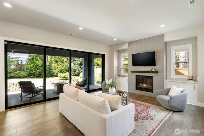 This bright and inviting living room offers seamless indoor-outdoor flow with full-length sliding glass doors that open to a private patio retreat. A sleek gas fireplace, lovely built-ins, and wide-plank wood floors create a cozy yet modern space for gathering or relaxing. | Image 7