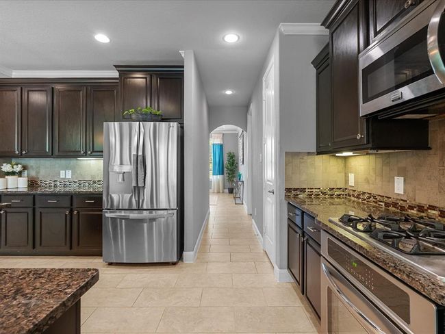 This modern kitchen features dark wood cabinetry, granite countertops, and stainless steel appliances, including a gas stove and microwave. The backsplash combines neutral tiles with a decorative border. The space is well-lit and opens into a cozy dining area. | Image 11