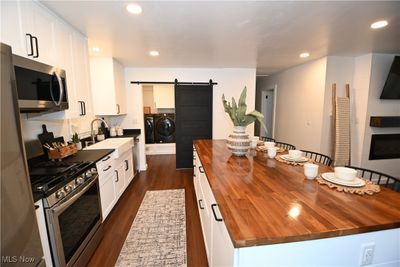 Kitchen with stainless steel appliances, island with butcher block countertop, and a barn door separating the laundry area. | Image 2