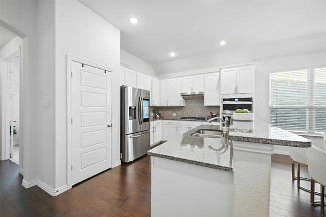 Kitchen with dark wood-type flooring, backsplash, light stone counters, stainless steel fridge, and recessed lighting | Image 8