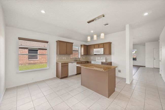 Kitchen featuring white appliances, a center island, a sink, tasteful backsplash, and light tile patterned flooring | Image 7
