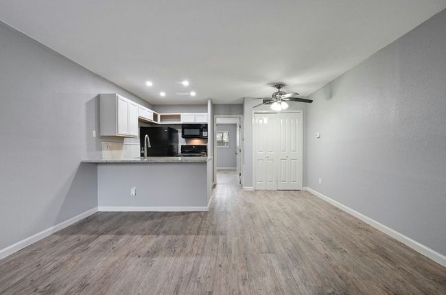 Kitchen featuring white cabinetry, a peninsula, light wood finished floors, black appliances, and recessed lighting | Image 7