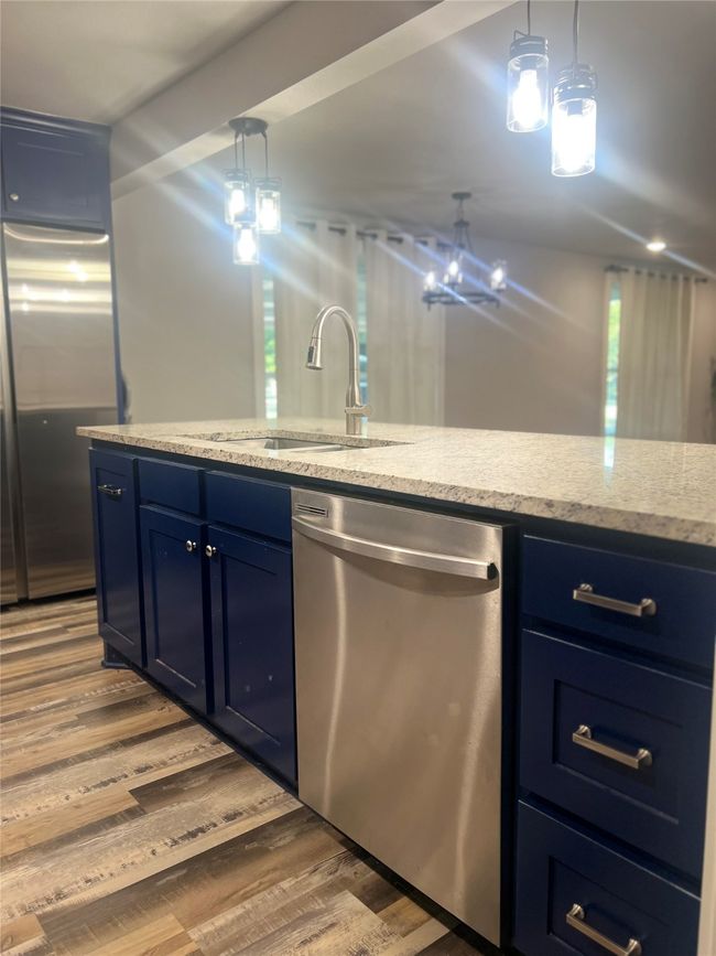 Kitchen with blue cabinets, stainless steel appliances, wood finished floors, light stone countertops, and hanging light fixtures | Image 4