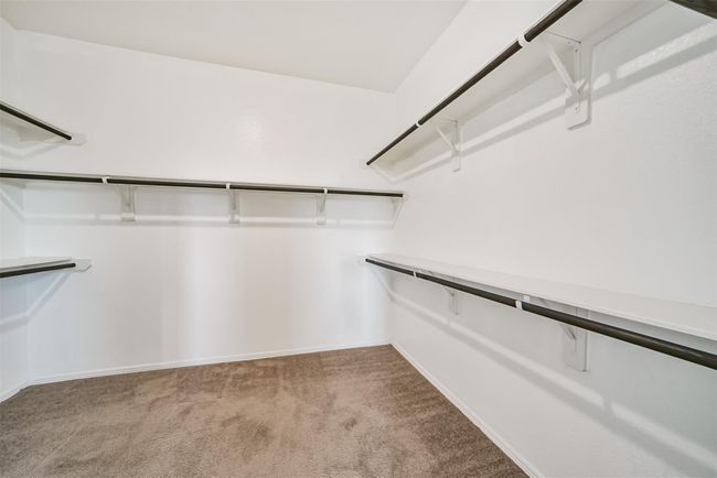 This photo shows a spacious walk-in primary closet with multiple shelves and hanging rods, featuring neutral carpeting and white walls for a clean, organized look. | Image 14