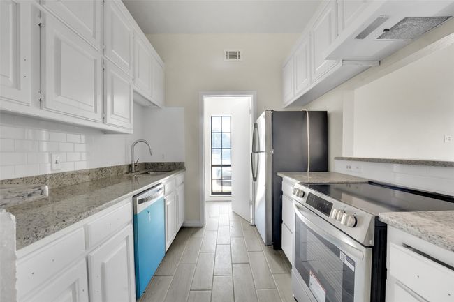 Kitchen with appliances with stainless steel finishes, white cabinets, wall chimney range hood, tasteful backsplash, and light stone countertops | Image 5