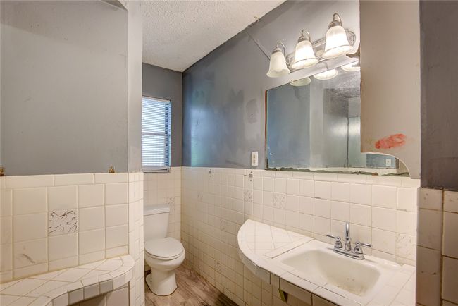 Bathroom featuring tile walls, toilet, a textured ceiling, a sink, and wood finished floors | Image 28