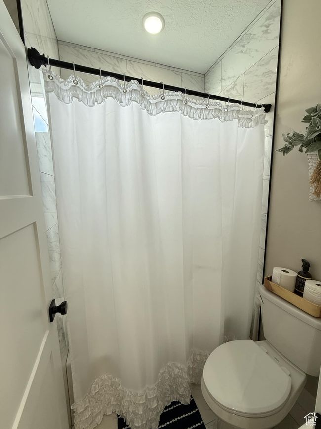 Full bathroom featuring a shower with shower curtain, toilet, and a textured ceiling | Image 62