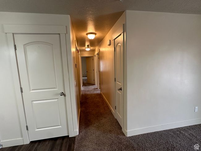 Corridor with dark colored carpet, a textured ceiling, and baseboards | Image 10