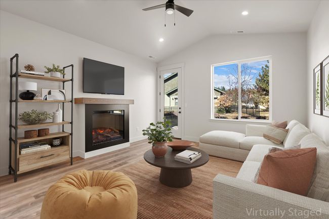 Living room with vaulted ceiling, a ceiling fan, a glass covered fireplace, light wood-style flooring, and visible vents | Image 5