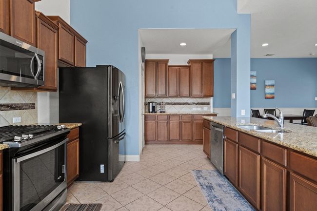 Kitchen featuring appliances with stainless steel finishes, a sink, light tile patterned flooring, light stone counters, and decorative backsplash | Image 4