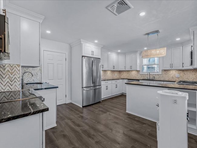 Kitchen featuring appliances with stainless steel finishes, a sink, backsplash, white cabinetry, and dark wood finished floors | Image 4