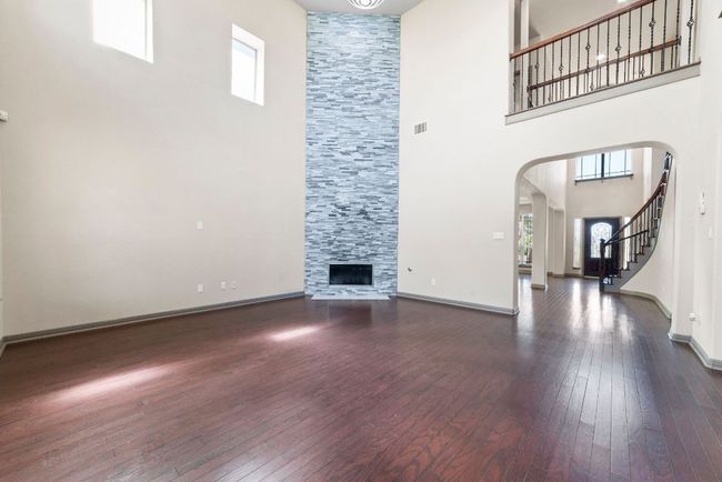Unfurnished living room featuring arched walkways, a high ceiling, dark wood-style floors, a tiled fireplace, and stairway | Image 11