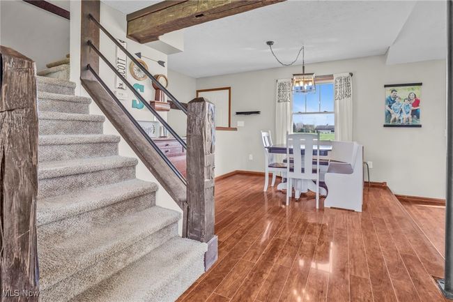 Dining space with beamed ceiling, a chandelier, baseboards, wood finished floors, and stairs | Image 9