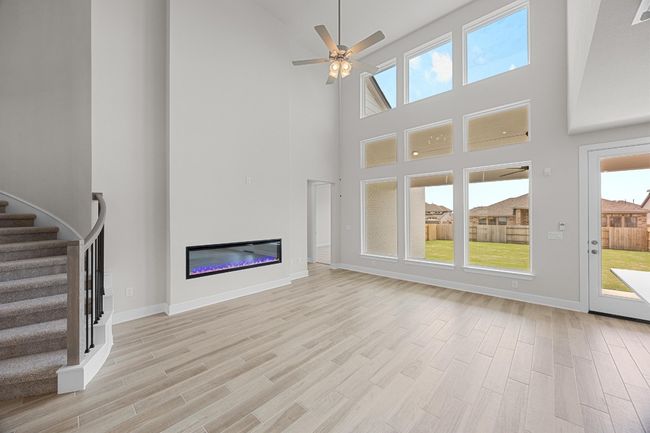 Unfurnished living room featuring a towering ceiling, stairway, light wood-type flooring, a ceiling fan, and a glass covered fireplace | Image 6