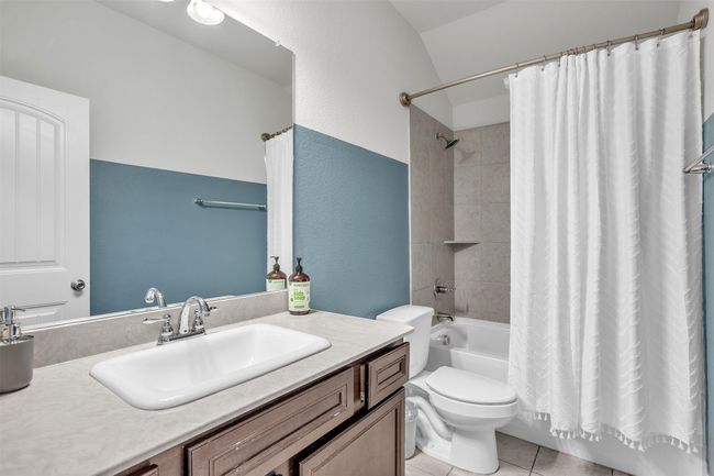 Bathroom featuring vanity, shower / bathtub combination with curtain, tile patterned floors, lofted ceiling, and a textured wall | Image 24