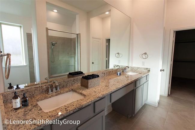 This bathroom features a spacious double vanity with granite countertops, sleek fixtures, and ample storage. It includes a spacious walk in glass-enclosed shower, creating a modern and airy feel. | Image 5