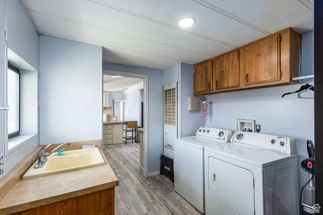 Washroom with separate washer and dryer, a textured ceiling, cabinet space, light wood finished floors, and a sink | Image 17