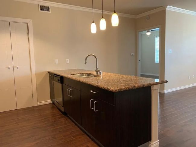 Kitchen featuring a peninsula, dark wood finished floors, stainless steel dishwasher, light stone counters, and ornamental molding | Image 20