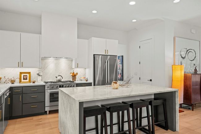 Kitchen featuring stainless steel appliances, light stone counters, light wood-style floors, a breakfast bar, and recessed lighting | Image 13