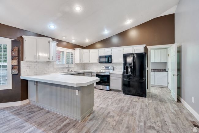 Kitchen with backsplash, vaulted ceiling, a sink, black appliances, and a peninsula | Image 6