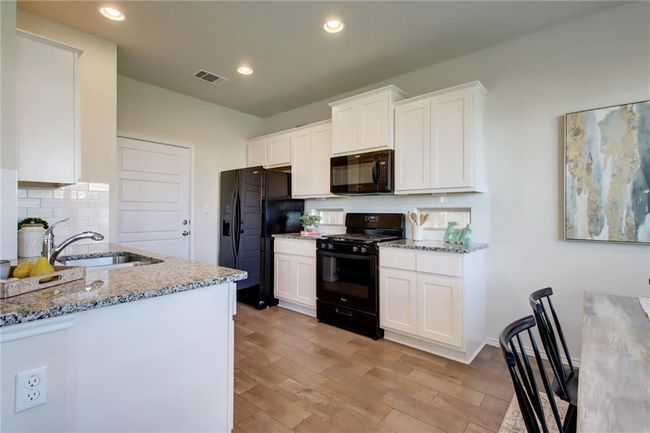 Kitchen with black appliances, light stone counters, white cabinets, and recessed lighting | Image 9