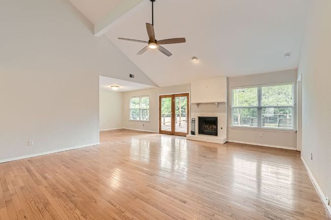 Unfurnished living room with beamed ceiling, high vaulted ceiling, a large fireplace, a ceiling fan, and light wood finished floors | Image 5