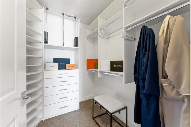 This photo shows a spacious, organized walk-in closet featuring white shelving and drawers, ample hanging space. It's perfect for keeping clothes and accessories neatly stored. | Image 16