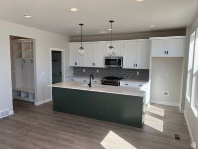 Kitchen featuring white cabinetry, a kitchen island with sink, stainless steel appliances, and decorative light fixtures | Image 3