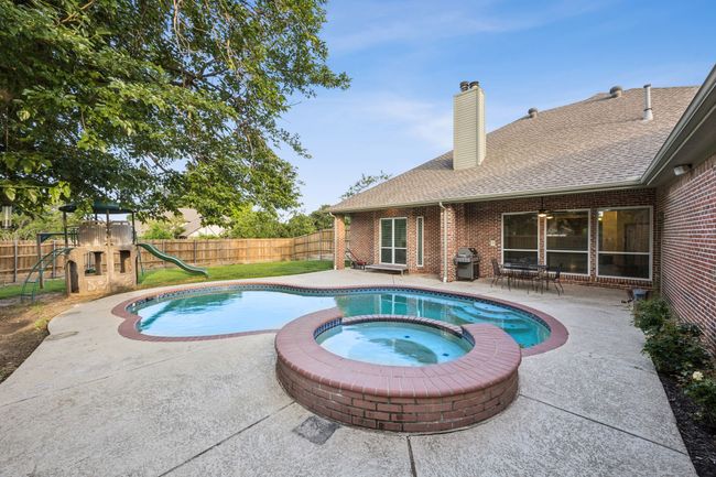 View of swimming pool featuring a large fenced backyard, a covered patio with a ceiling fan, and a pool with connected hot tub | Image 28