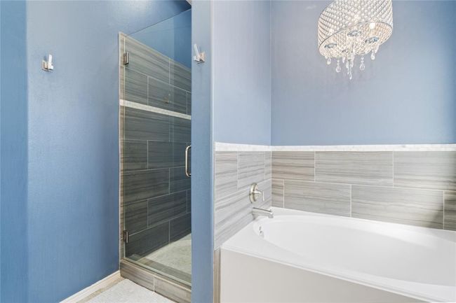 This bathroom features a sleek, modern design with blue walls, a luxurious soaking tub, and a glass-enclosed shower. The space is enhanced by elegant tile work and a chic chandelier, offering a spa-like atmosphere. | Image 32