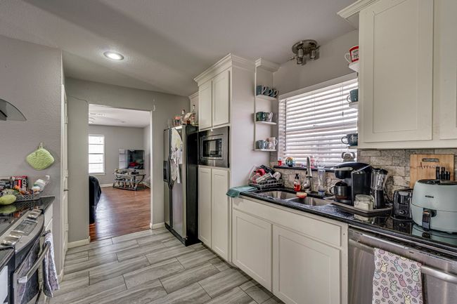 Kitchen featuring dark countertops, wood tiled floor, decorative backsplash, stainless steel appliances, and a sink | Image 15