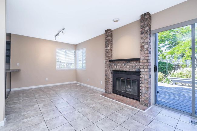 Unfurnished living room featuring light tile patterned floors, baseboards, visible vents, a brick fireplace, and track lighting | Image 11